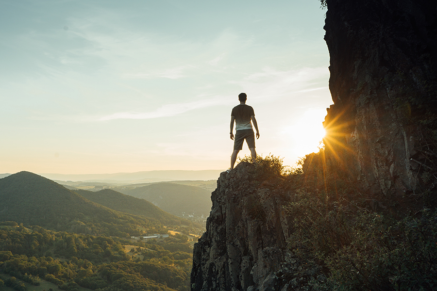 A person on a cliff, staring at a sunrise