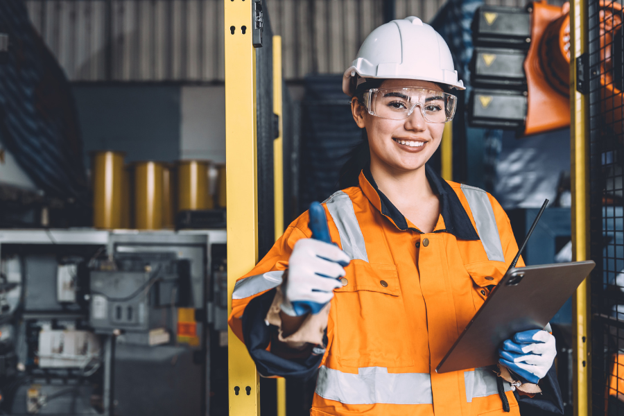A smiling manufacturing employee with a hard hat and orange vest