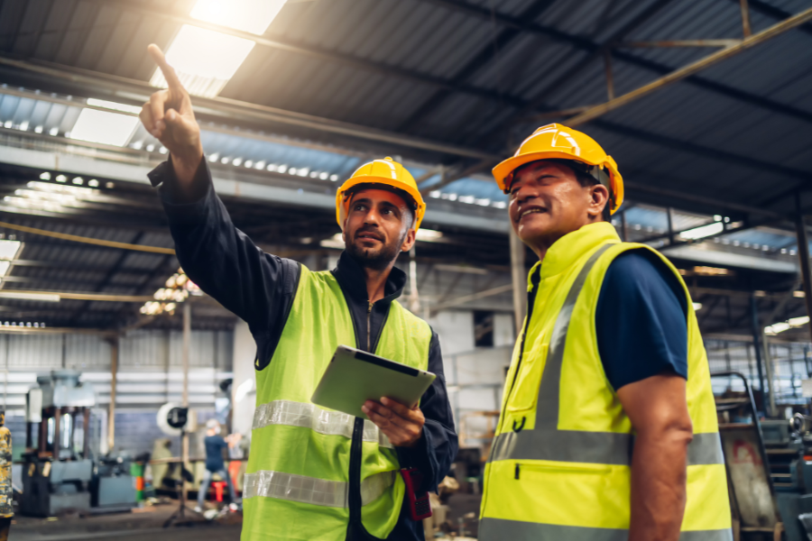 Two manufacturing employees with yellow hard hats and vests